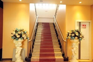 A hotel staircase with a red carpet, flanked by white columns with floral arrangements. - Juli Boutique Hotel (Kunming Jinma Zhengchang Fruit Market Juhua Subway Station) (Kunming)