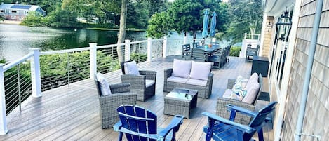 A wooden deck with outdoor furniture, a view of a lake, and a white railing.