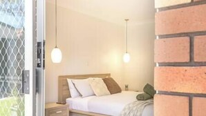 A bedroom with a wooden bed, white bedding, and two pendant lights. - Private Pool | Sleeps 12 | Pets | Basketball Hoop (Coffs Harbour)