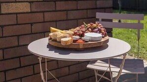 A round table with a variety of cheeses and fruits on a wooden board, set against a brick wall. - Private Pool | Sleeps 12 | Pets | Basketball Hoop (Coffs Harbour)