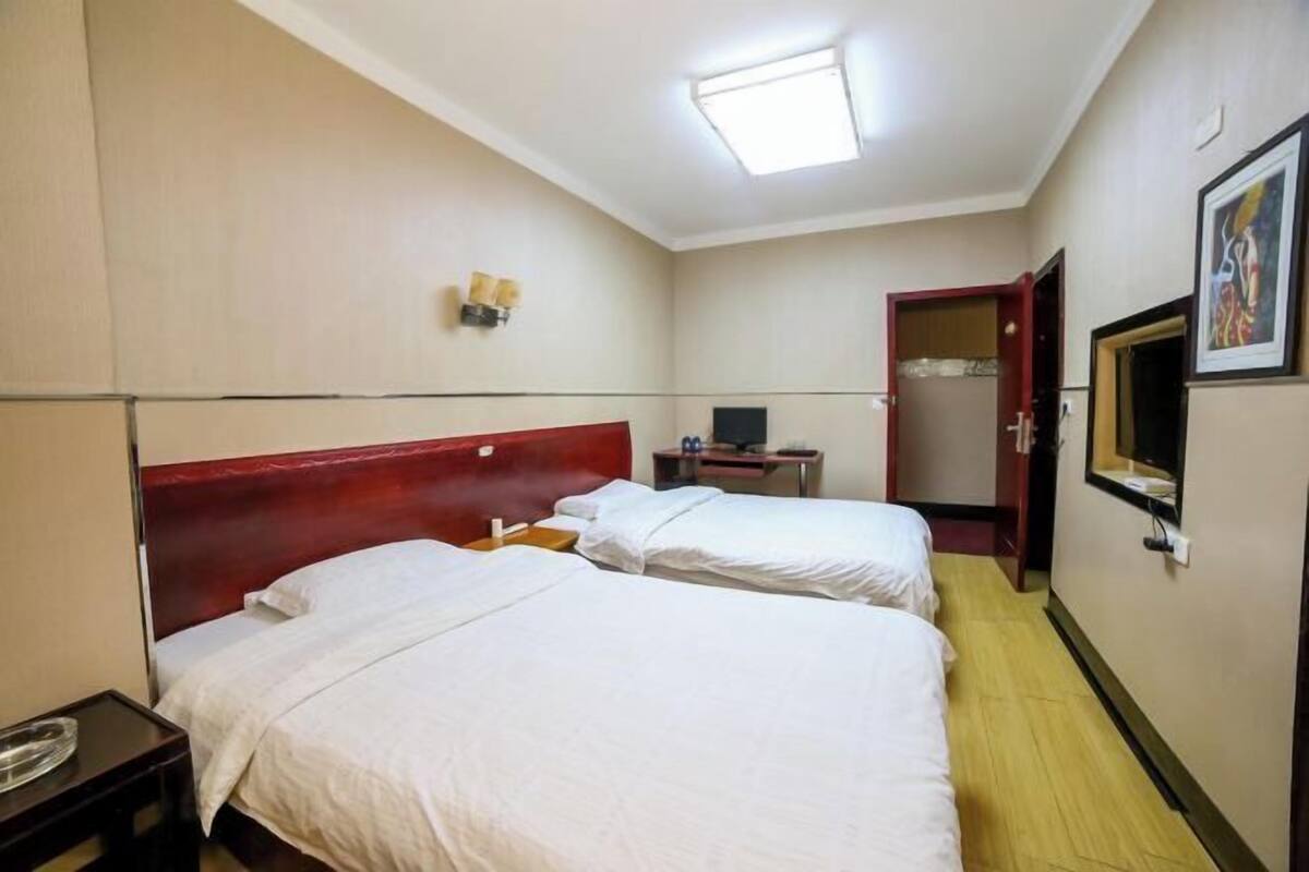 Una habitación de hotel con dos camas, un escritorio, un televisor y un espejo en la pared.