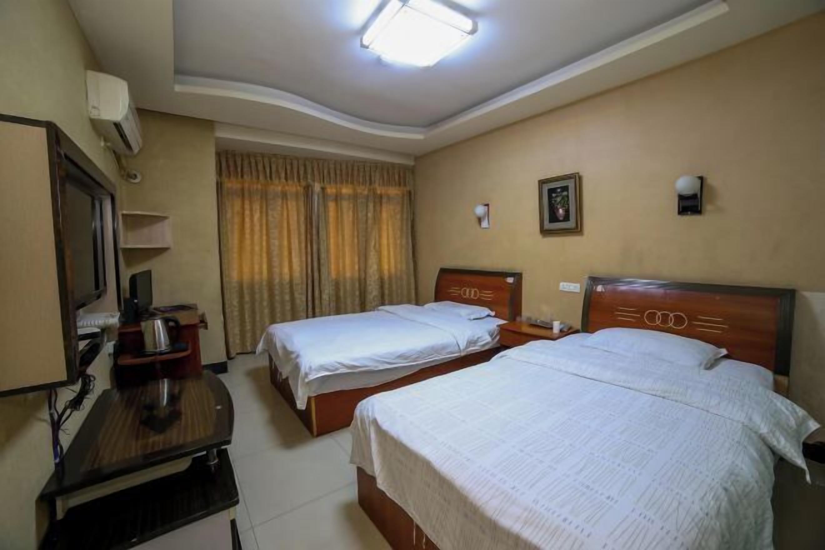 A hotel room with two single beds, a desk with a chair, a television, and a window with curtains.