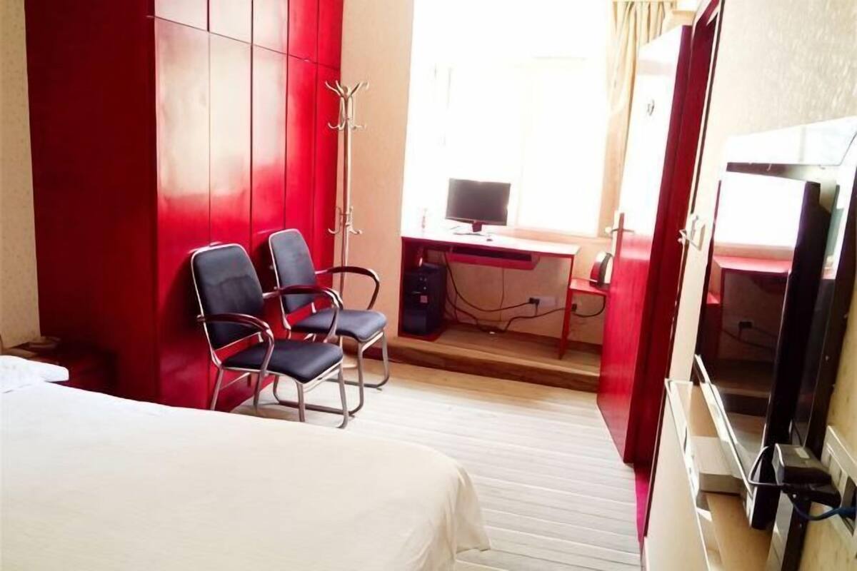 Una habitación de hotel con una cama, dos sillas, un escritorio con una computadora y un televisor.