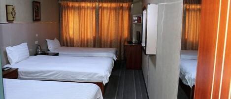 Une chambre d’hôtel avec trois lits simples, une petite table, un téléviseur et une armoire.