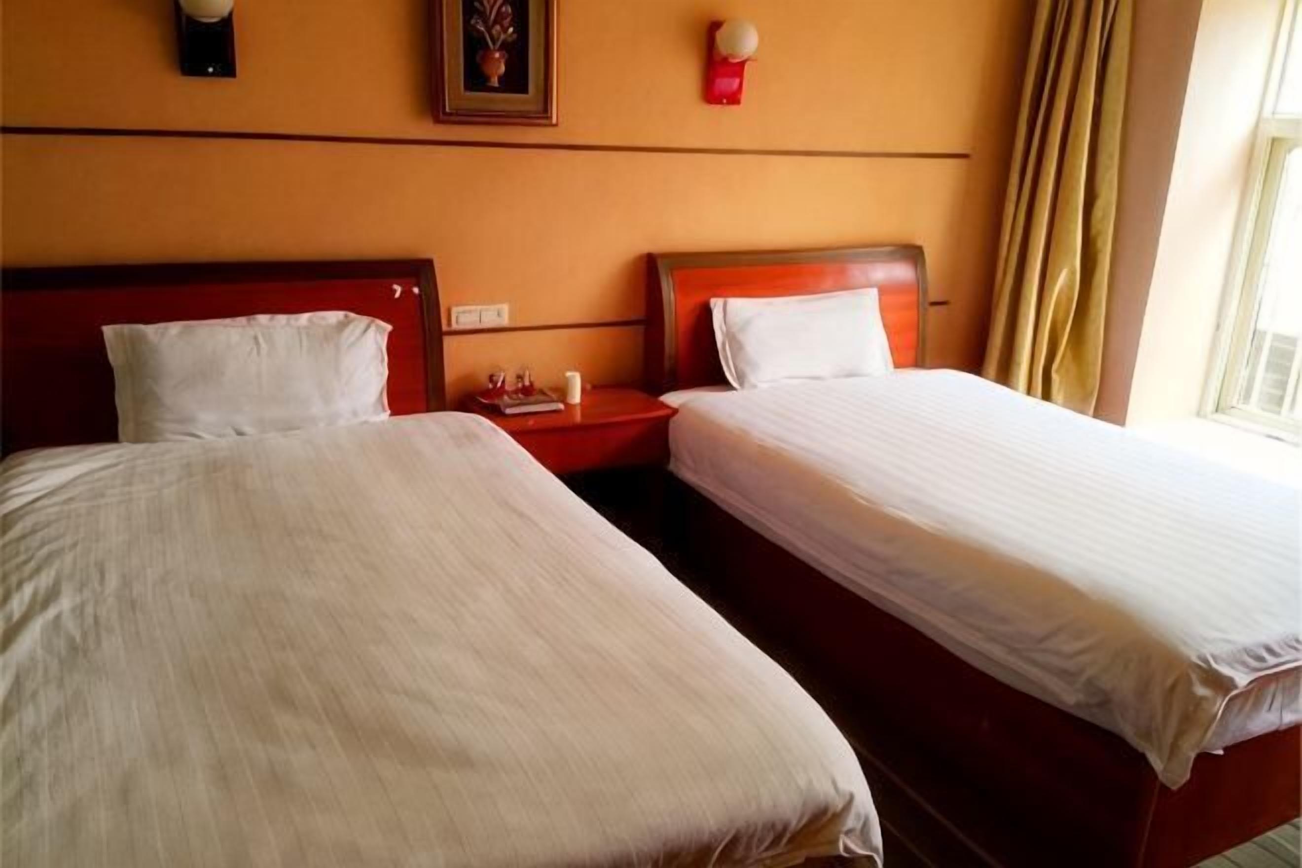 Two single beds with wooden headboards, a nightstand with a lamp, and a window with curtains.
