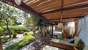 A covered outdoor seating area with wooden flooring, a cushioned bench, and hanging plants. - Gambá Casa Boutique (Búzios)