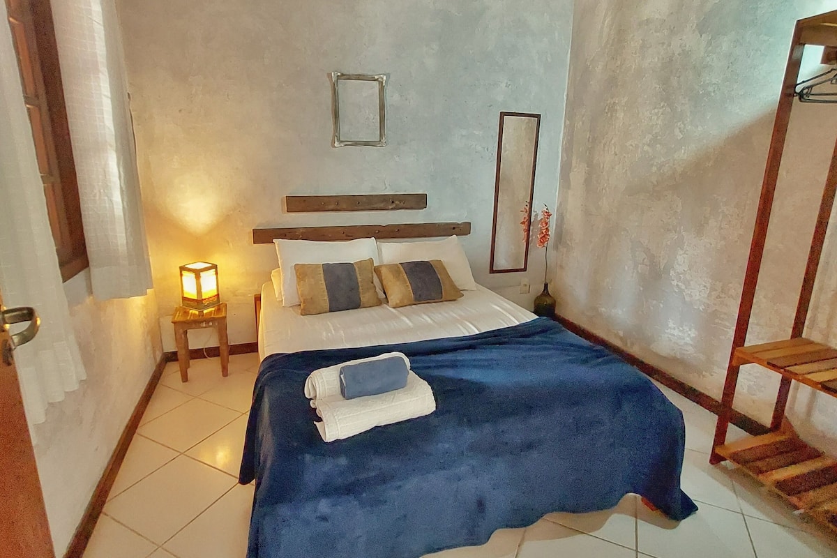 Ein Schlafzimmer mit einem Bett, einem Deckenventilator, einem Nachttisch mit Lampe und einem Holzregal.