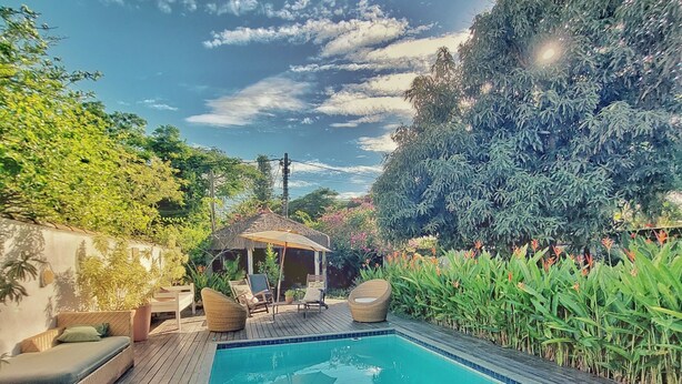 A rectangular pool with a wooden deck, surrounded by lush greenery and a thatched-roof gazebo. - Gambá Casa Boutique (Búzios)