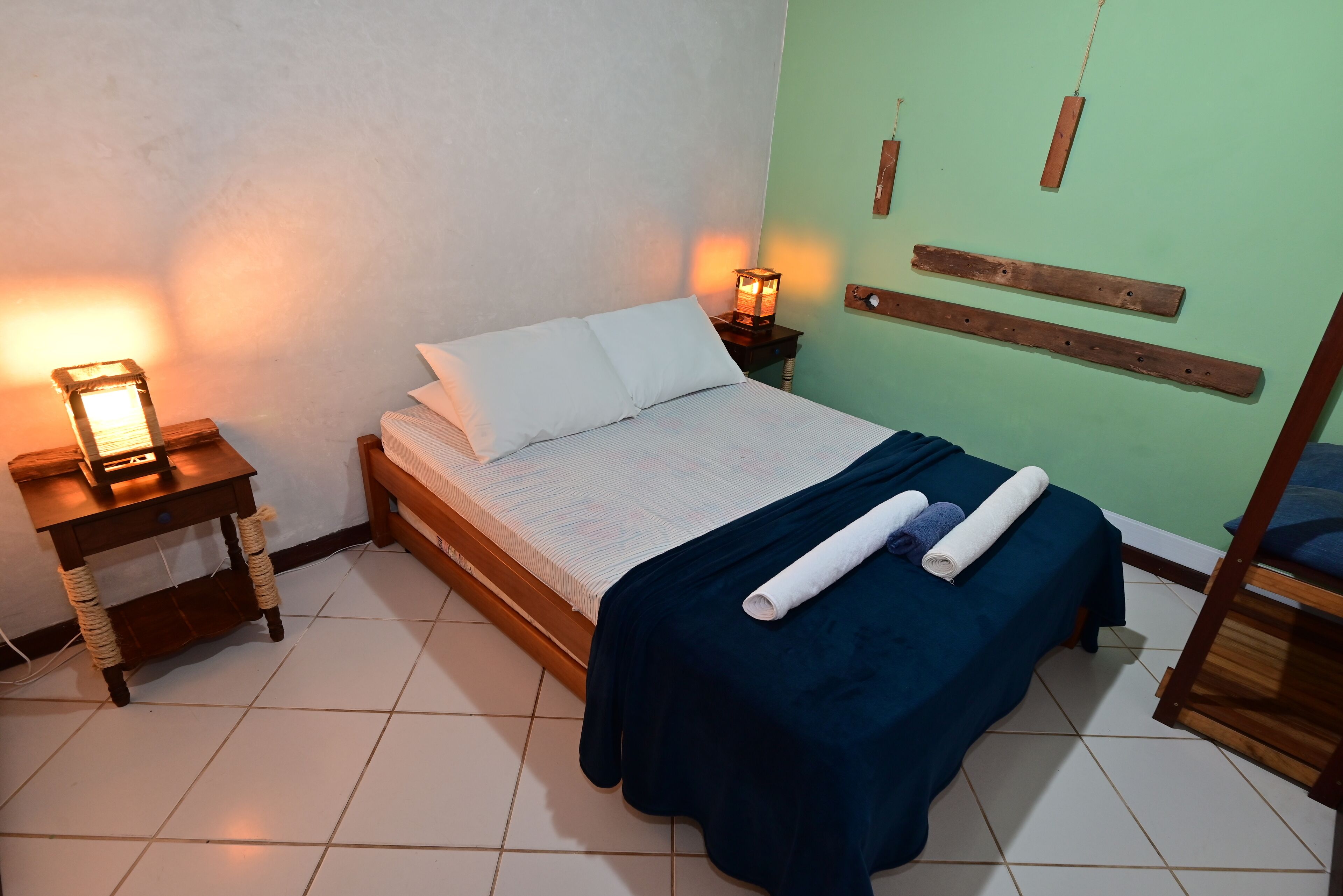 Un lit bien fait, avec une couverture bleue et des serviettes enroulées, une table de chevet avec une lampe et une tête de lit en bois.