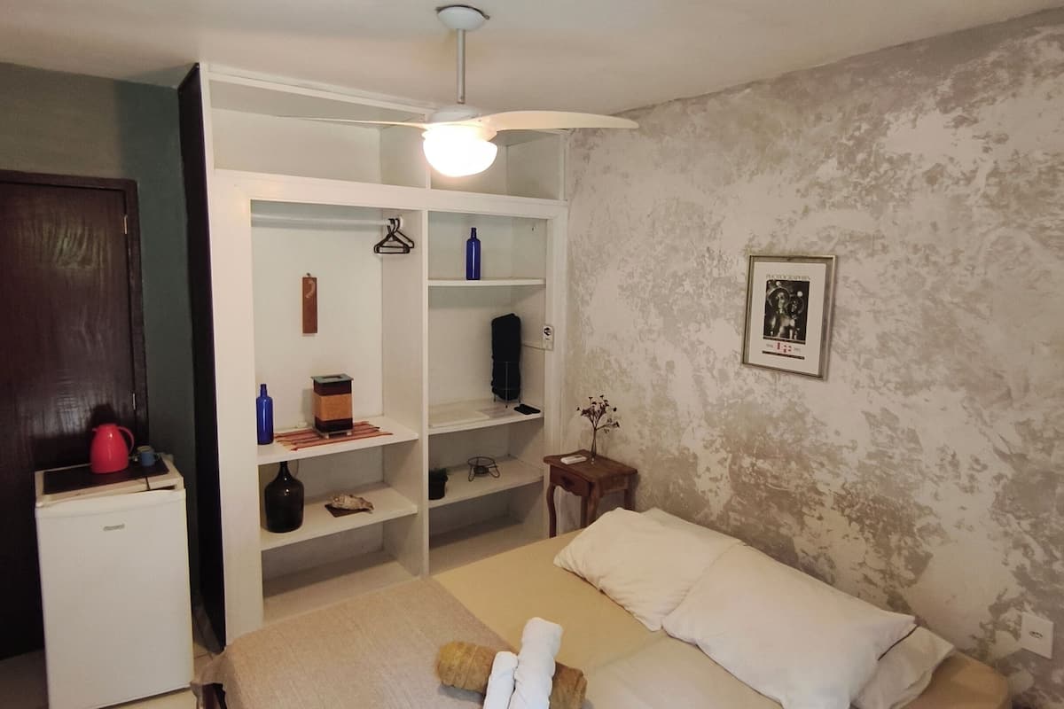 Ein Schlafzimmer mit Bett, Kleiderschrank, einem kleinen Tisch und Deckenventilator.
