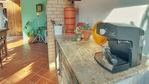 A kitchen with a coffee machine, potted plants, and a brick wall. - Gambá Casa Boutique (Búzios)