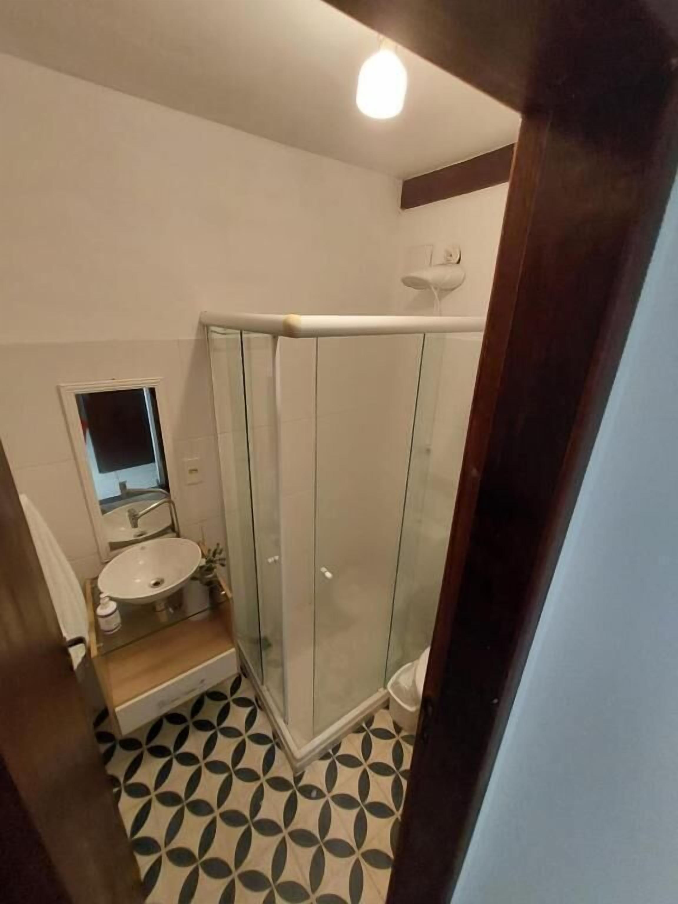 A modern bathroom with a glass shower enclosure, a sink with a mirror, and a patterned floor.