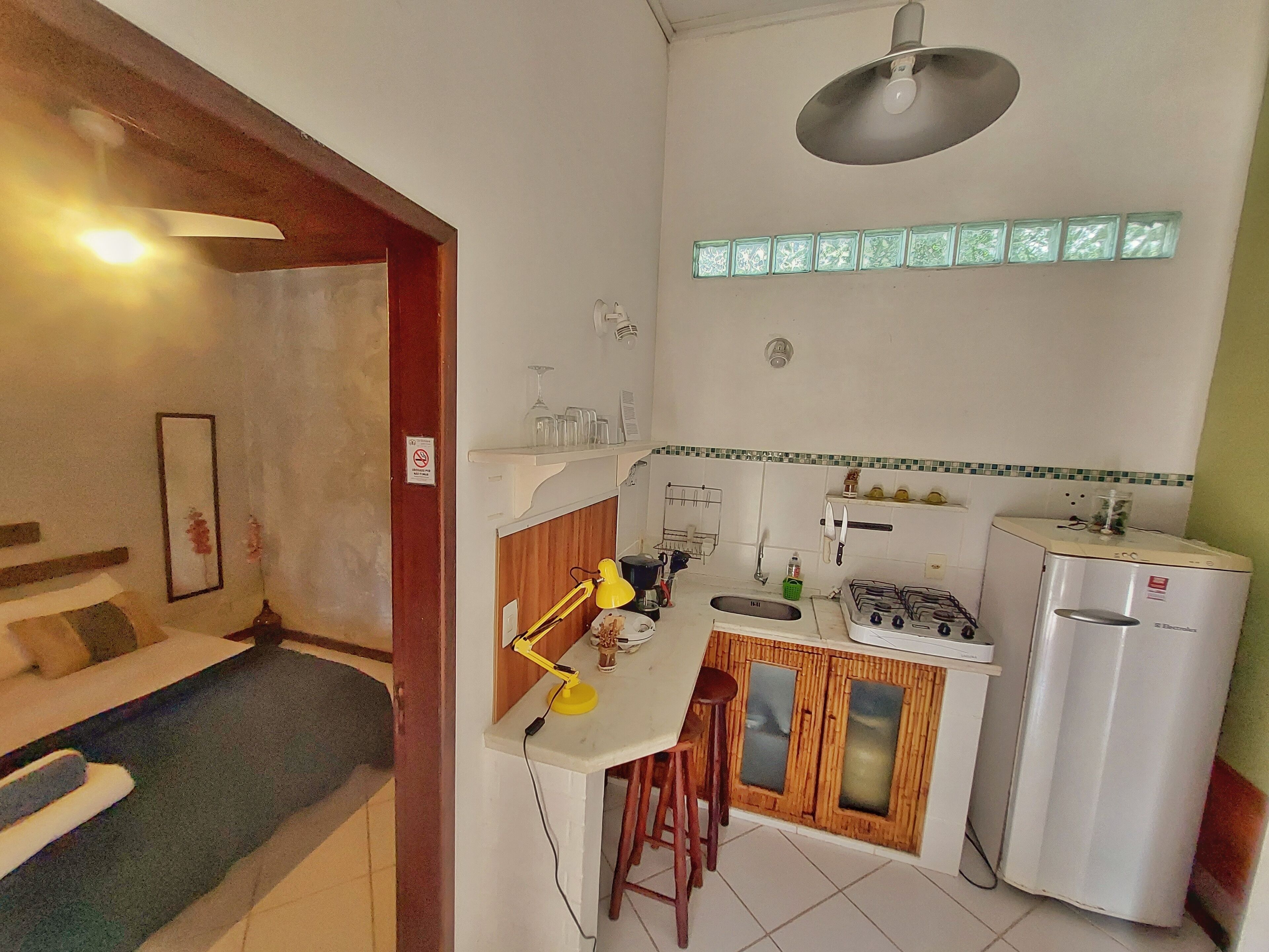 A compact kitchen with a gas stove, sink, and a refrigerator. There is a small bar area with stools and a table lamp.