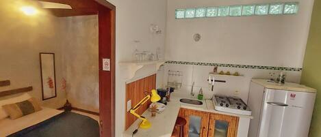 A compact kitchen with a gas stove, sink, and a refrigerator. There is a small bar area with stools and a table lamp.