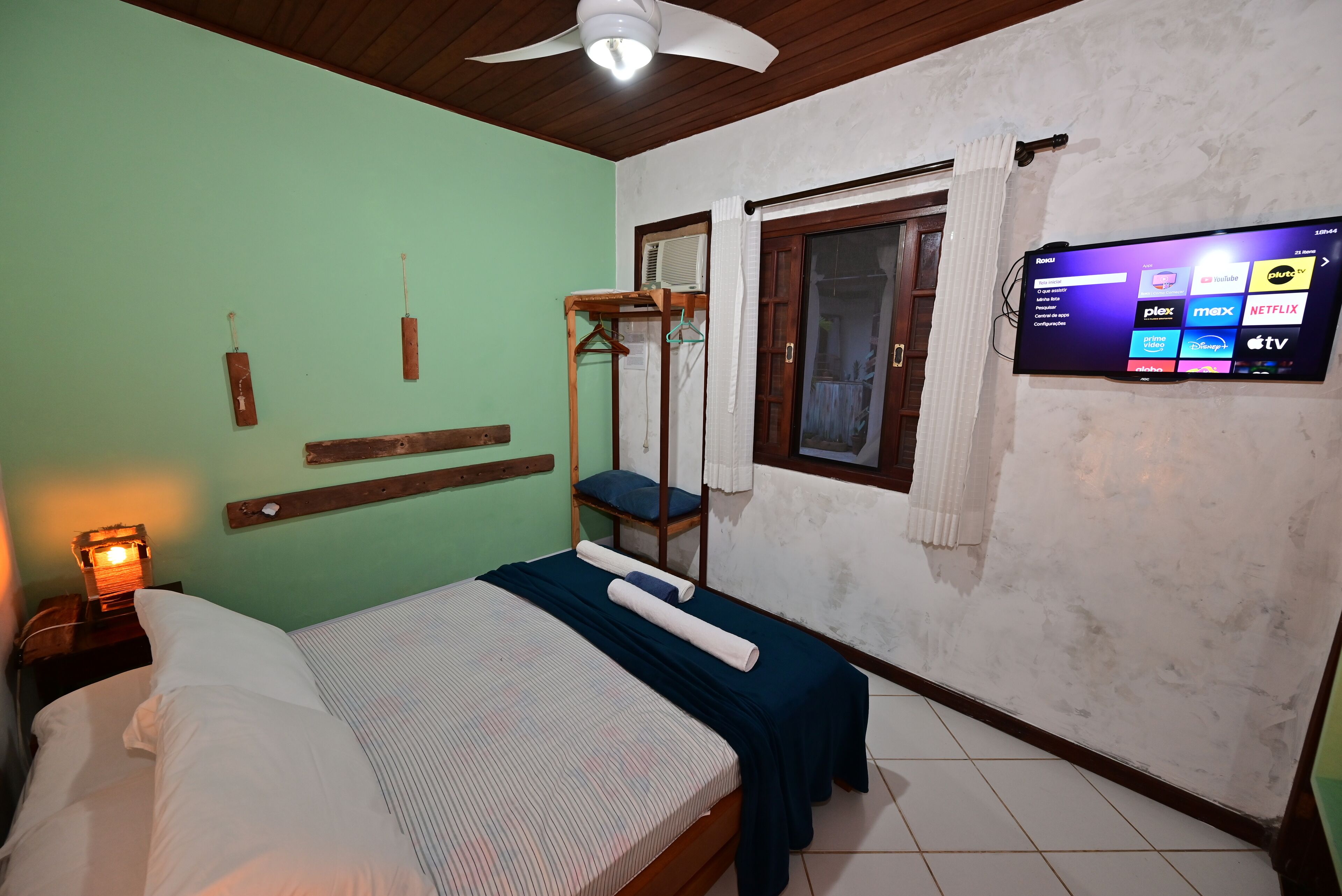 A hotel room with a bed, a wooden bunk bed, a TV mounted on the wall, and a window with curtains.