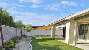 A residential backyard with artificial grass, a white brick wall, and a covered patio area. - Spacious 4-bedroom single level house with  RV parking in Jurupa Valley (Jurupa Valley)