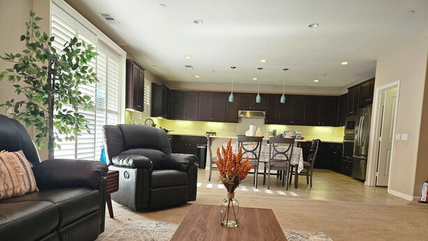 A modern living room with a black leather sofa, a wooden coffee table, and a dining area with a table and chairs. - Spacious 4-bedroom single level house with  RV parking in Jurupa Valley (Jurupa Valley)