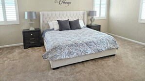 A bedroom with a tufted headboard, a patterned bedspread, two bedside tables with lamps, and a wall with a decorative phrase. - Spacious 4-bedroom single level house with  RV parking in Jurupa Valley (Jurupa Valley)