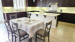 A modern kitchen with dark wooden cabinets, a central island with a white countertop, and a dining area with a table set for four. - Spacious 4-bedroom single level house with  RV parking in Jurupa Valley (Jurupa Valley)