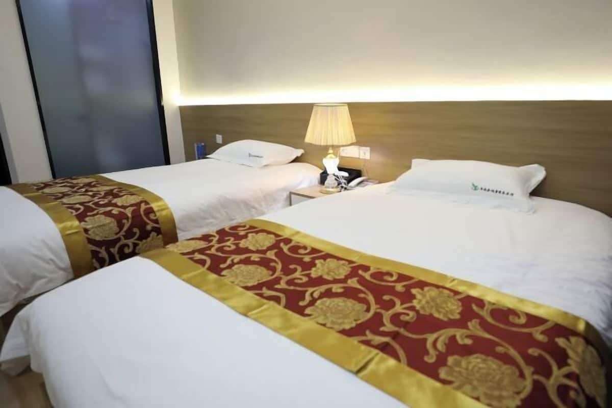 Une chambre d’hôtel avec deux lits, chacun recouvert d’une couverture blanche et rouge, une lampe de chevet et une table de chevet avec un téléphone.