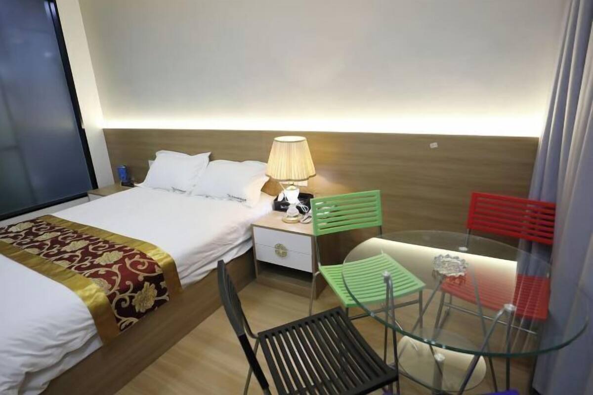 Une chambre d’hôtel avec un lit, une table de chevet, une lampe, des chaises vertes et rouges, et une table en verre.