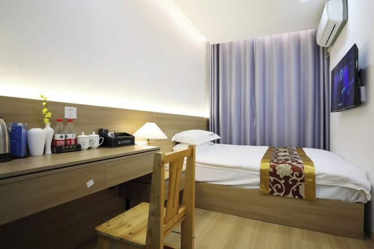 Une chambre d’hôtel avec un lit, un bureau, une chaise, une télévision et une fenêtre avec des rideaux.