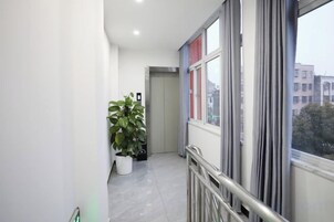 A narrow corridor with a potted plant, a door at the end, and a window with a view of buildings.