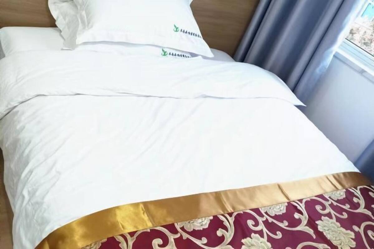 Un lit avec une literie blanche et une bordure dorée au pied du lit.