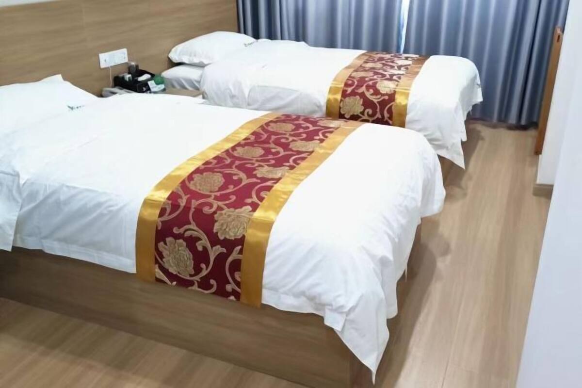 Une chambre d’hôtel avec deux lits, chacun agrémenté de draps blancs et d’une bande décorative rouge et or.