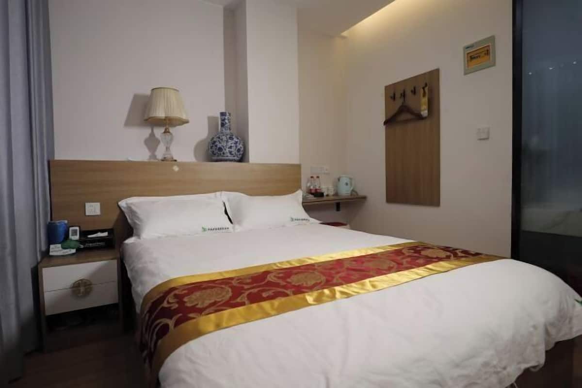 Une chambre d’hôtel avec un grand lit, une table de chevet, une lampe, un vase, un porte-manteau et un miroir.