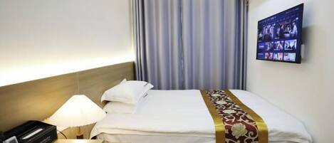 A hotel room with a bed, a bedside lamp, a TV mounted on the wall, and a window with curtains.