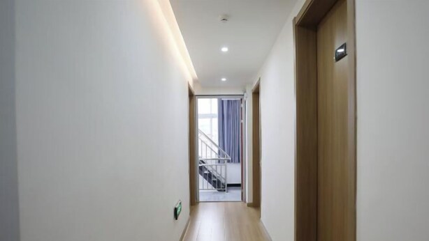 Un couloir avec un plancher en bois, des murs blancs et une porte sur le côté droit.