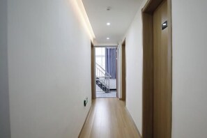 Un couloir avec un plancher en bois, des murs blancs et une porte sur le côté droit.