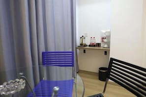 A small room with a blue chair, a black bench, a coffee machine, and a trash can.
