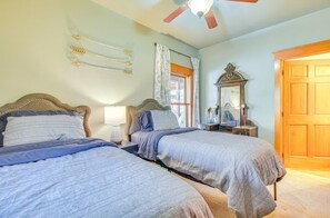 Ein Schlafzimmer mit zwei Betten, einem Deckenventilator, einem Fenster mit Vorhängen, einem Spiegel und einer Holztür.