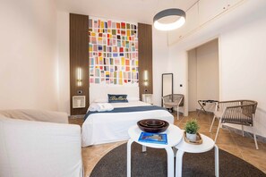 Une chambre d’hôtel moderne, équipée d’un lit, d’une petite table avec un bol et un livre, d’une chaise et d’un panneau décoratif mural.