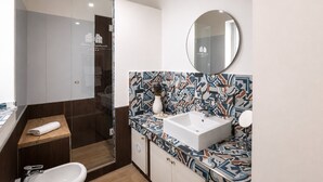Een moderne badkamer met een betegelde spatwand, een ronde spiegel en een witte wastafel.