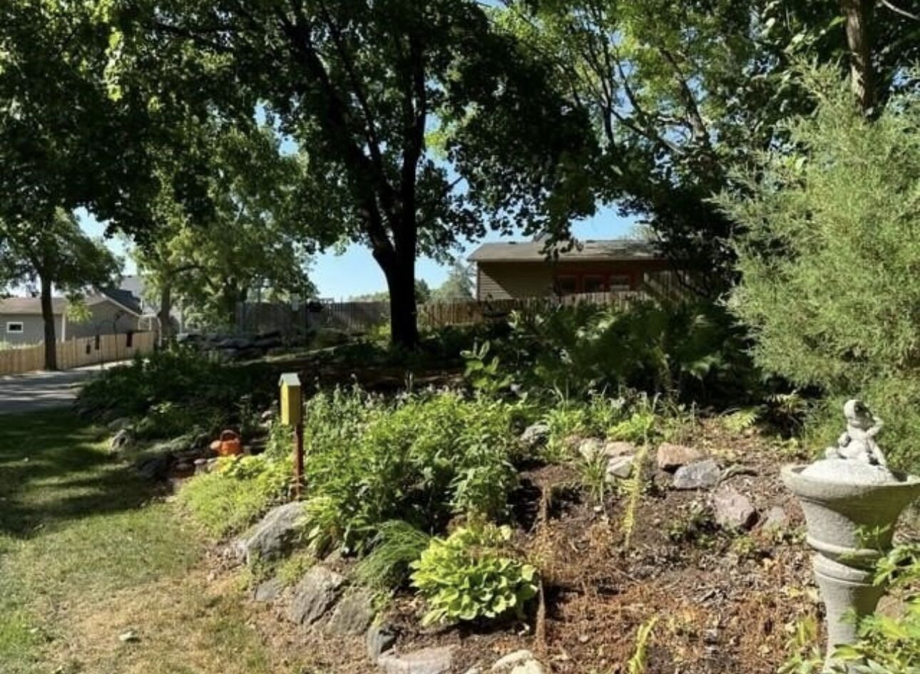 Ein Garten mit verschiedenen Pflanzen und einem Vogelbad aus Stein.
