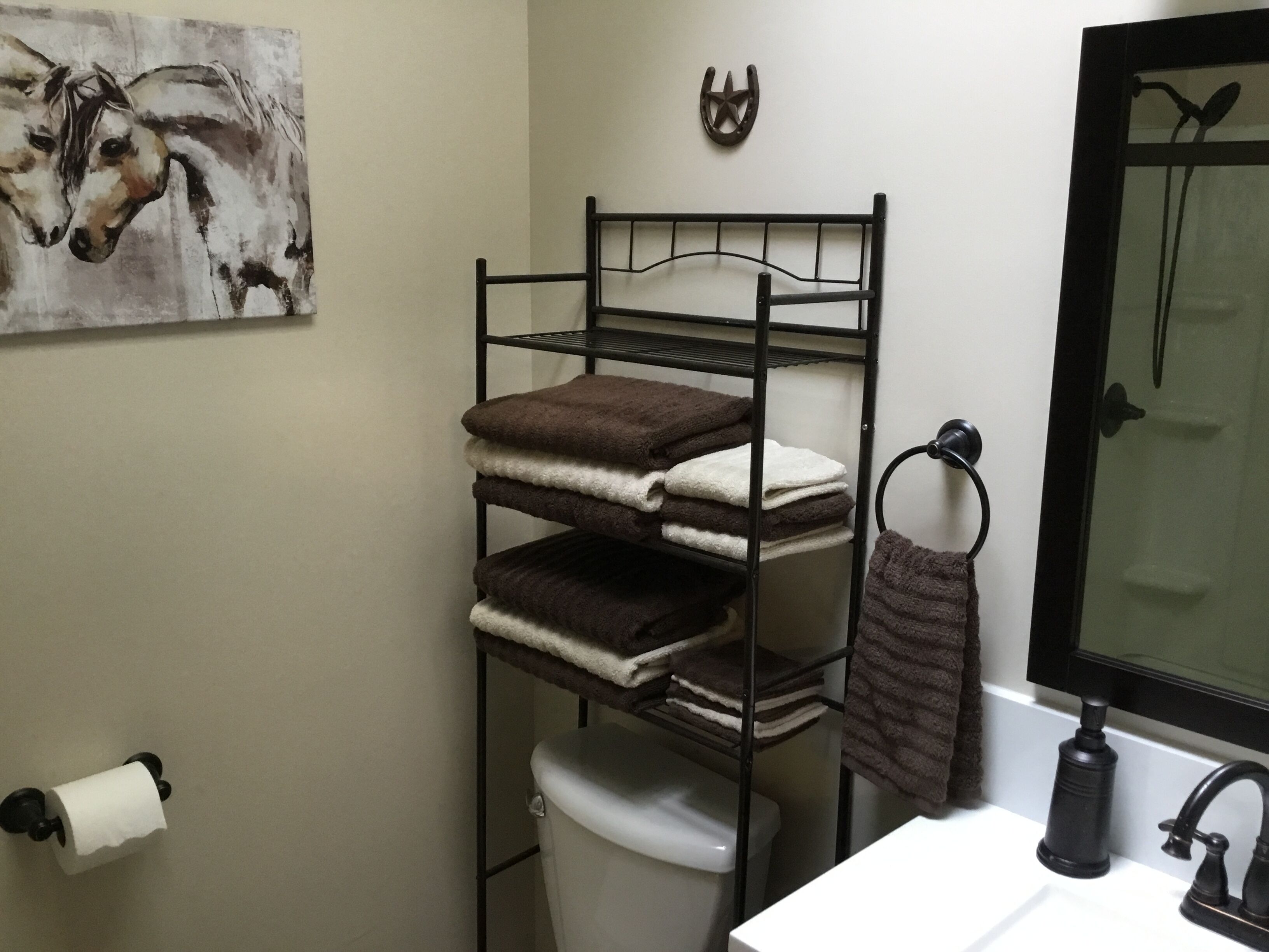 Ein Badezimmer mit einem schwarzen Metallregal, das Handtücher, eine Toilette und ein Waschbecken mit Armatur beherbergt.