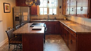 A kitchen with a central island, wooden cabinets, a refrigerator, and a window with a view.
