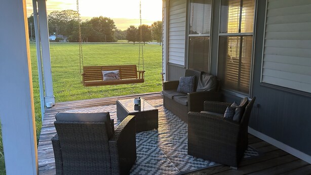 A porch with wicker furniture, a swing, and a view of a grassy field.
