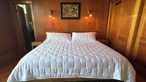 A large bed with a white quilt, two wall-mounted lamps, and a framed floral artwork above it.