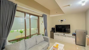 Ein Wohnzimmer mit grauem Sofa, weißem Couchtisch, Fernseher und Kühlschrank.