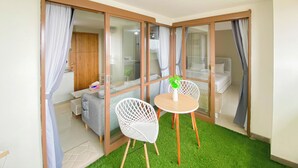 Ein Zimmer mit einer Schiebetür aus Glas, einem kleinen runden Tisch mit zwei weißen Stühlen, einem weißen Sofa und einem Bett mit weißem Kopfteil.