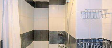Un espace douche équipé d’un pommeau de douche en métal, d’un rideau blanc et d’une étagère en métal.