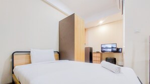A hotel room with a bed, a wooden wardrobe, a desk with a computer, and a TV on the wall. - Homey And Modern Studio Apartment B Residence (Pagedangan)