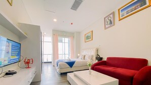 A modern hotel room with a bed, a red sofa, a white coffee table, and a TV on a white cabinet.