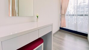A room with a large window, a mirror, and a small vase with flowers on a white console table.