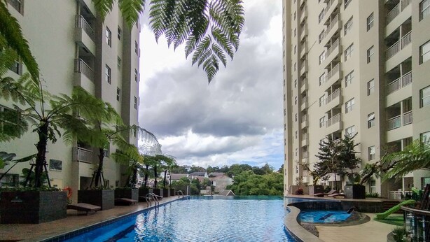 Une piscine entourée de grands immeubles, avec des palmiers et un ciel nuageux.