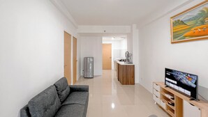 Una sala de estar moderna con un sofá gris, un televisor sobre un mueble de madera, una cocina al fondo y un cuadro en la pared.